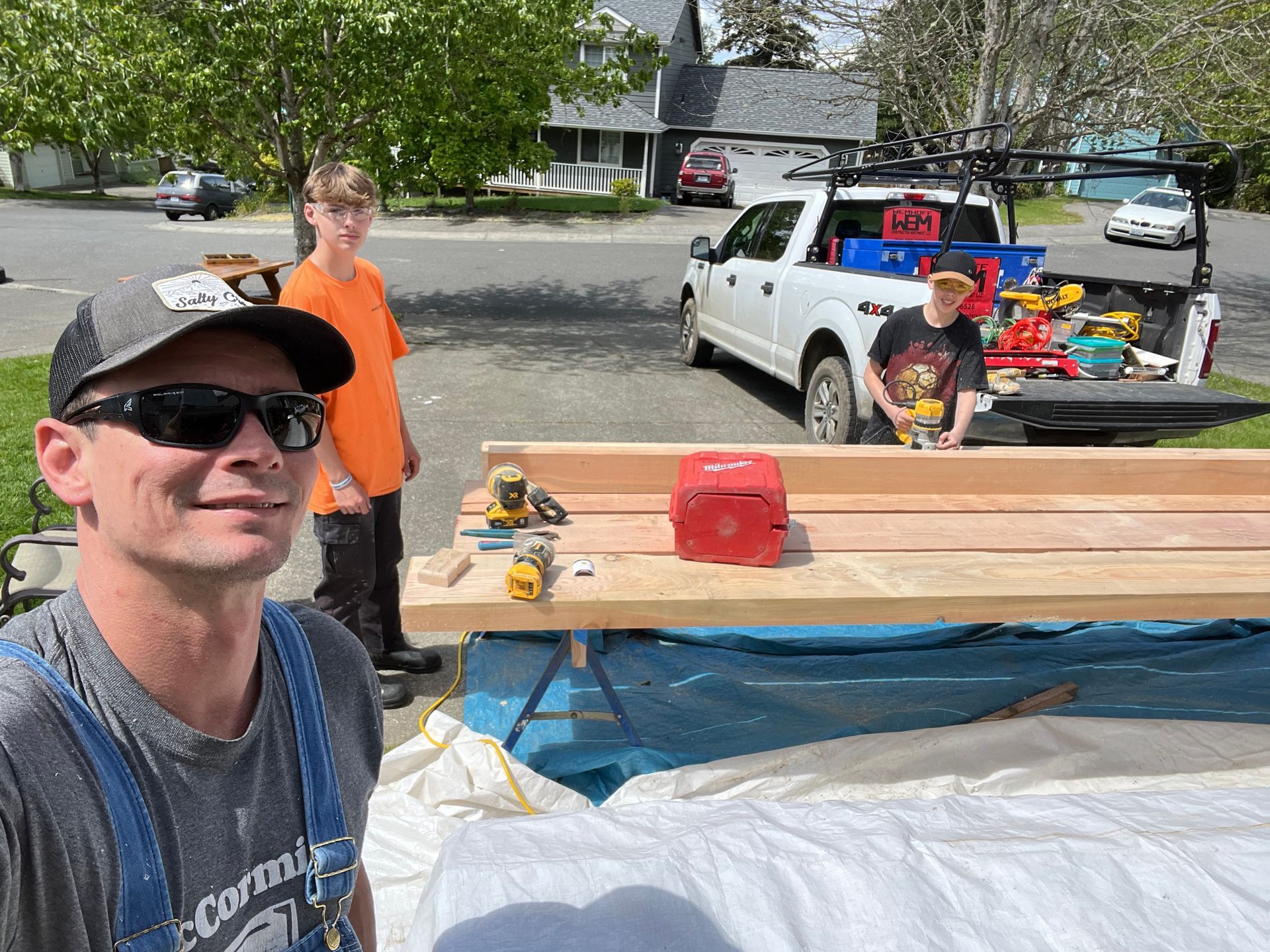A man is standing next to a wooden table in front of a truck.