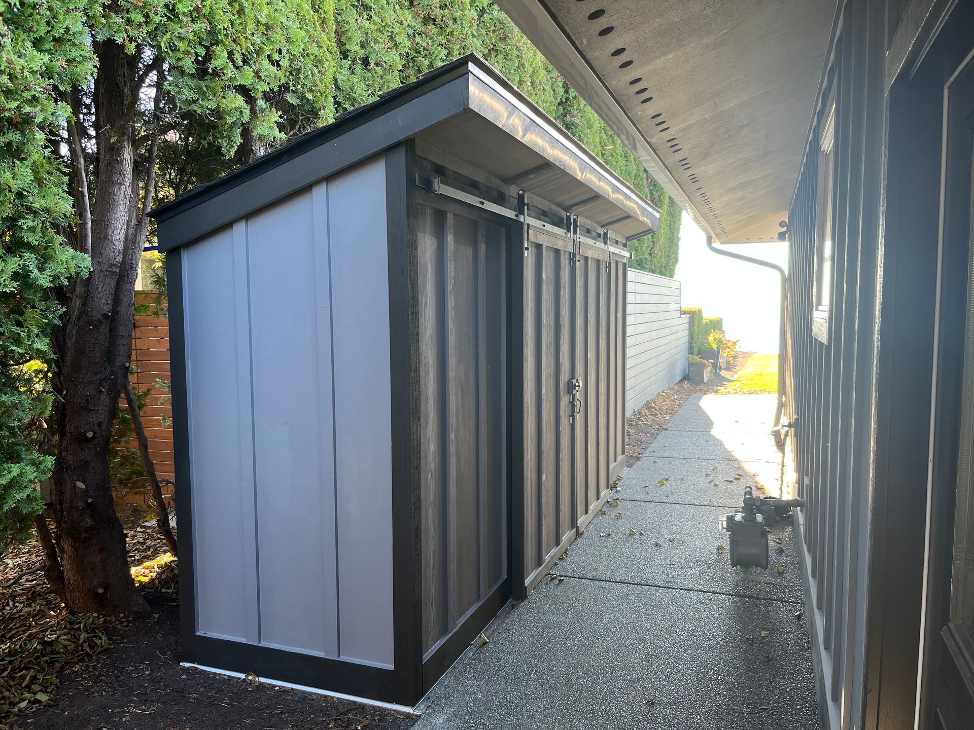A gray and black shed is sitting next to a house.