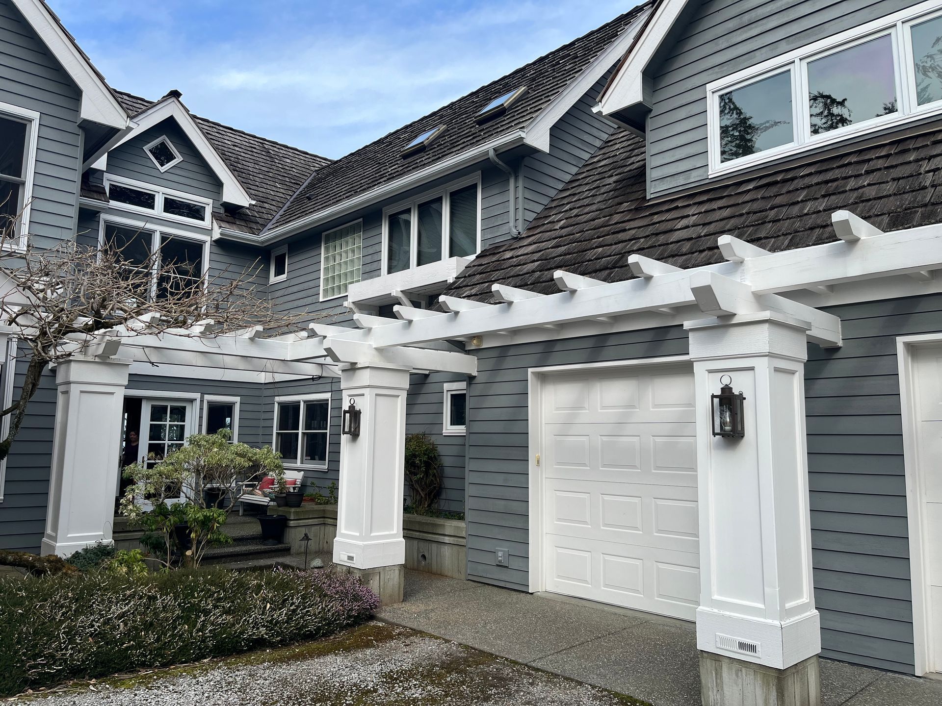 A large gray house with a white pergola and garage doors