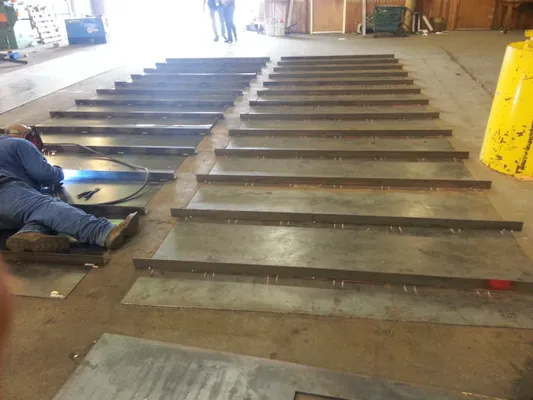 Warehouse floor with rows of metal beams laid out and a worker sitting on the left side
