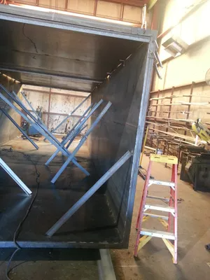 Open shipping container with blue X-braced supports in a warehouse, next to a ladder.