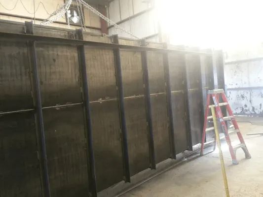 Large black metal enclosure in a warehouse, with a red ladder leaning against it under bright overhead lights.