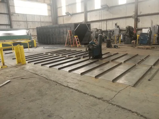 Worker standing among large metal beams in an industrial warehouse