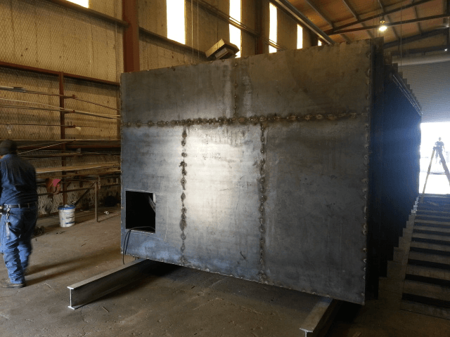 Large metal industrial tank being assembled inside a warehouse, with a worker nearby.