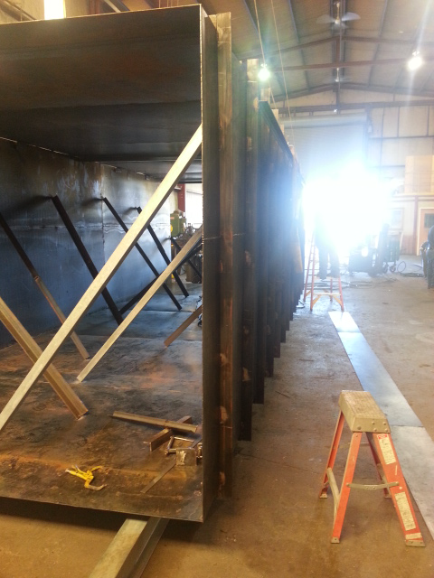 Construction site with large metal structure, wooden braces, ladder, and bright light in the background