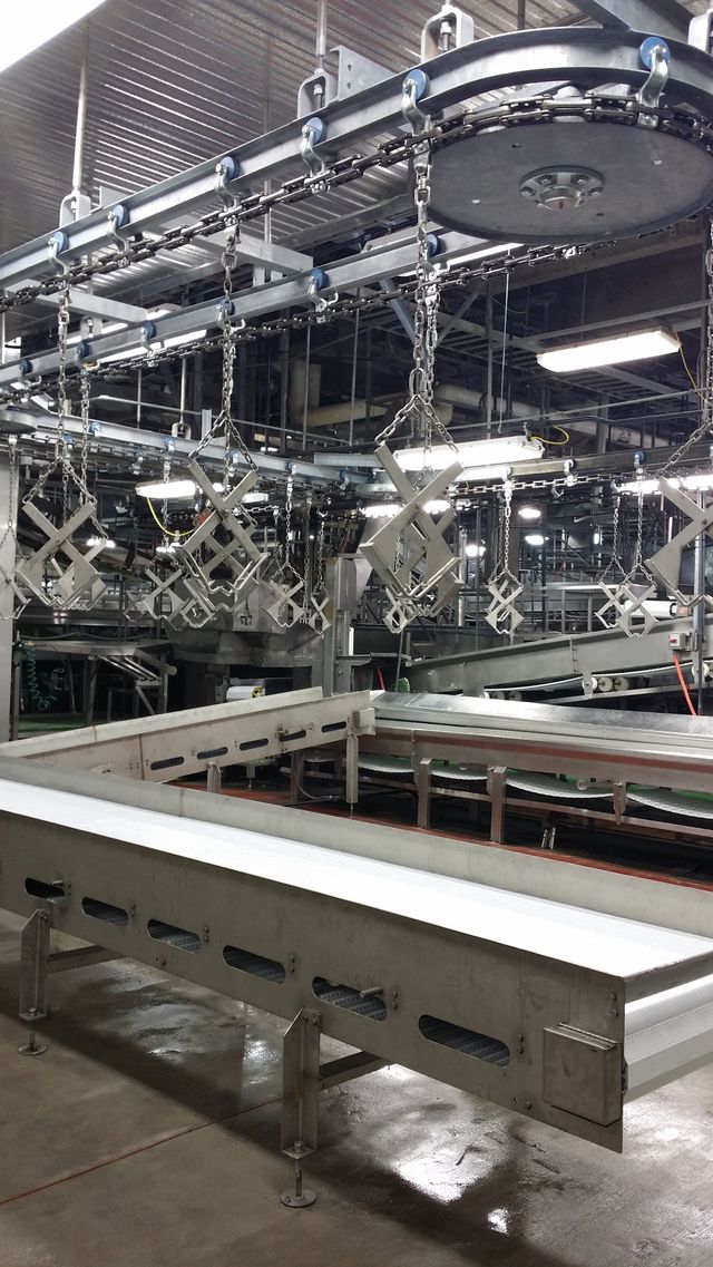 Industrial factory line with large metal machinery and a white conveyor table in the foreground.
