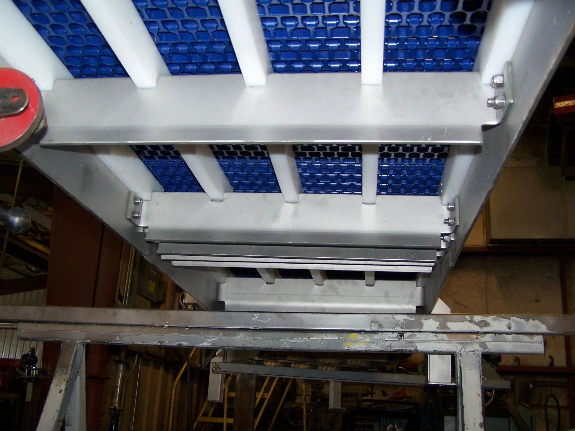 Looking up at a metal and blue industrial conveyor or ladder structure with beams and rollers