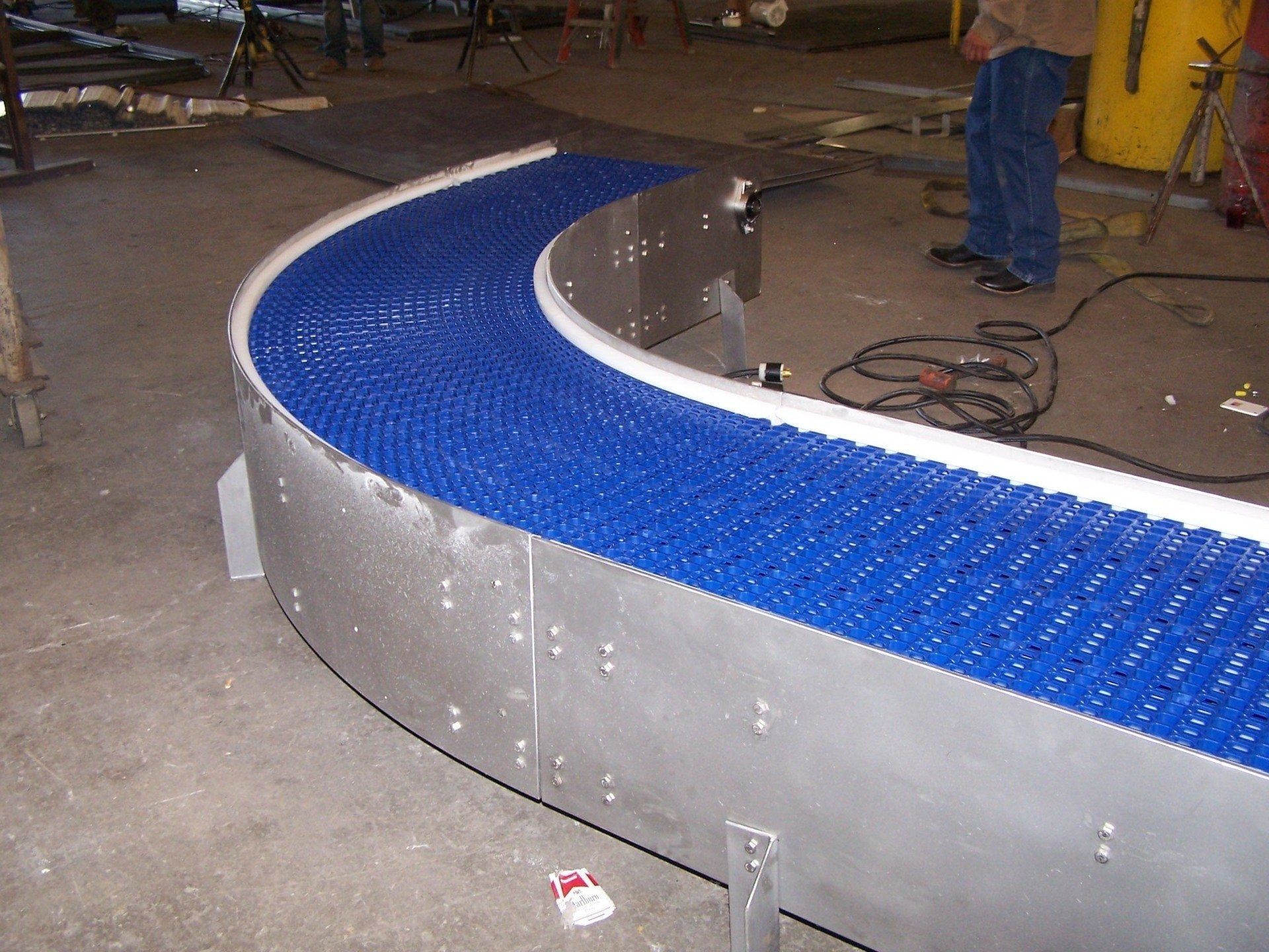 Curved blue conveyor belt with silver sides in an industrial workshop