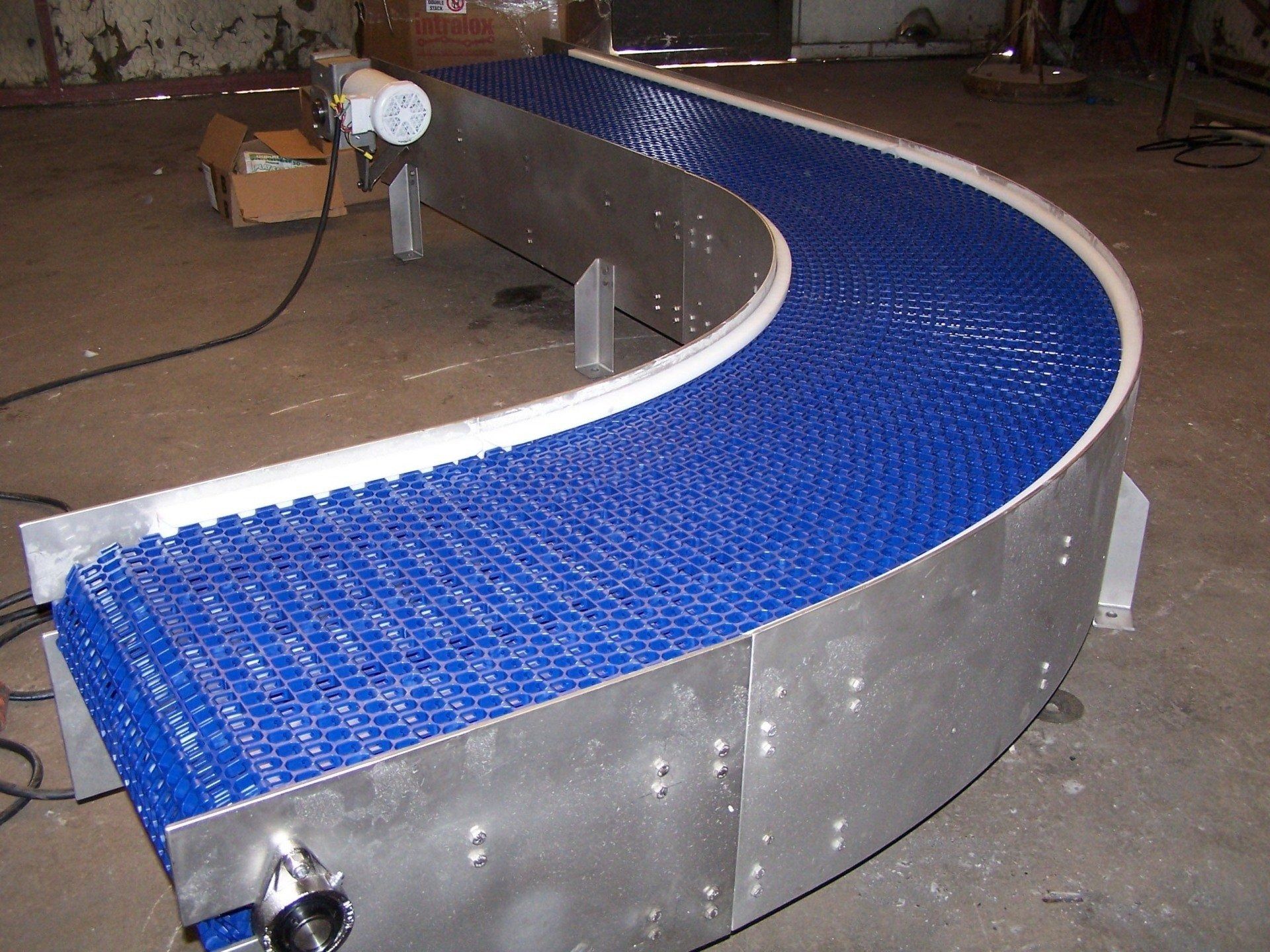 Curved blue conveyor belt with silver sides in an industrial workshop