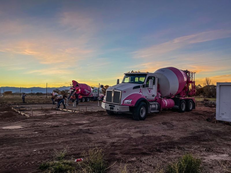 A pink concrete mixer truck is parked in a dirt field.