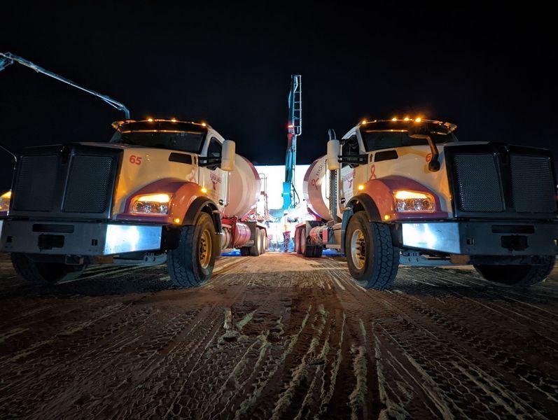 Two trucks are parked next to each other on a dirt road at night.