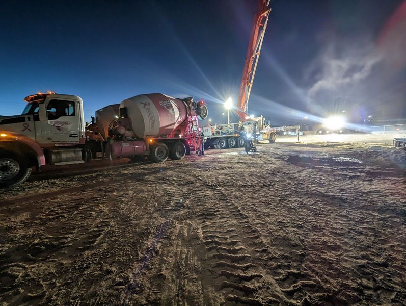 A concrete mixer truck is driving down a dirt road at night.