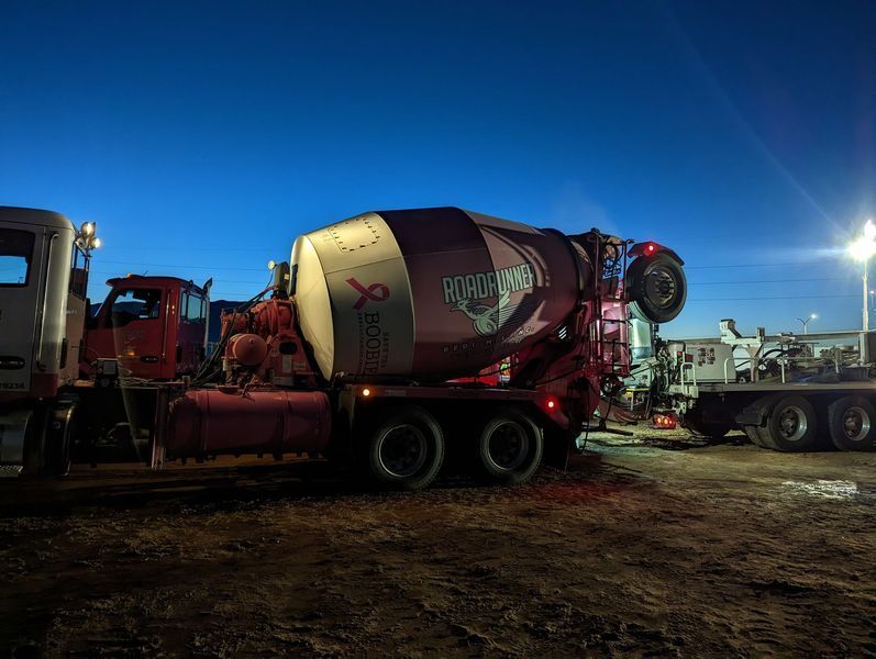 A concrete mixer truck is parked in a dirt lot at night.