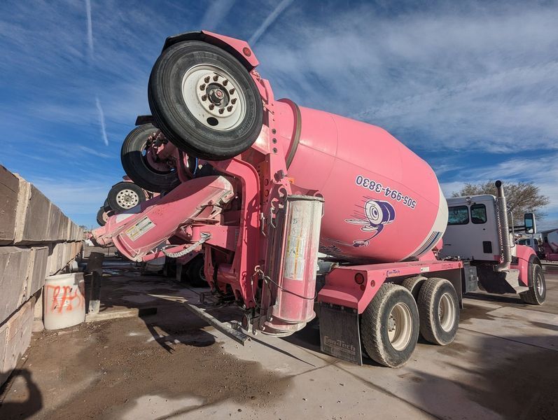 A pink concrete mixer truck is parked on the side of the road.