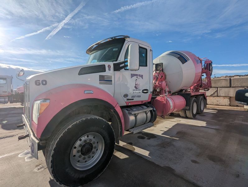 A pink and white concrete mixer truck is parked in a parking lot.