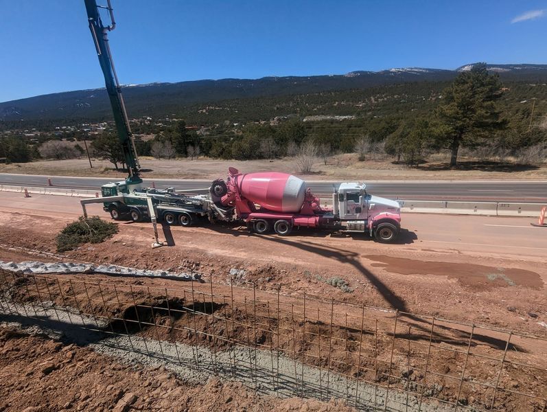 A concrete mixer truck is driving down a dirt road.