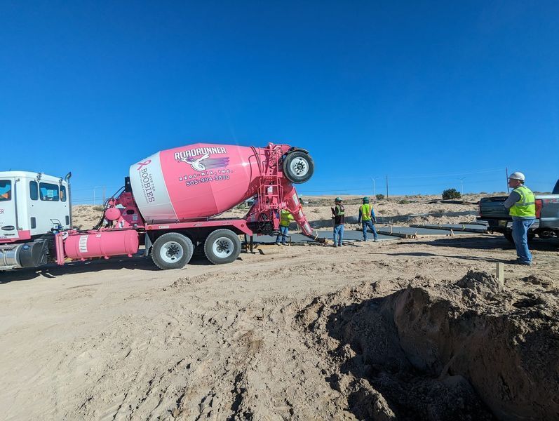 A pink concrete mixer truck is being loaded with concrete