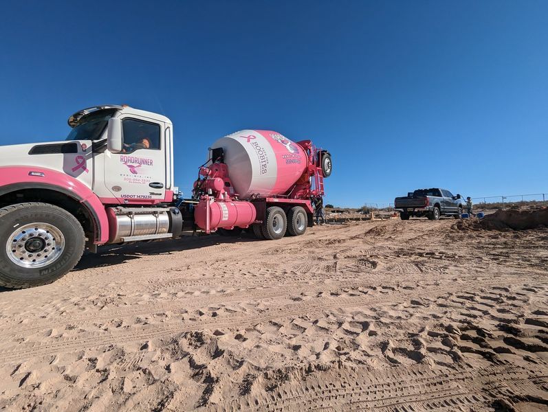 A pink and white concrete mixer truck is parked on a dirt road.