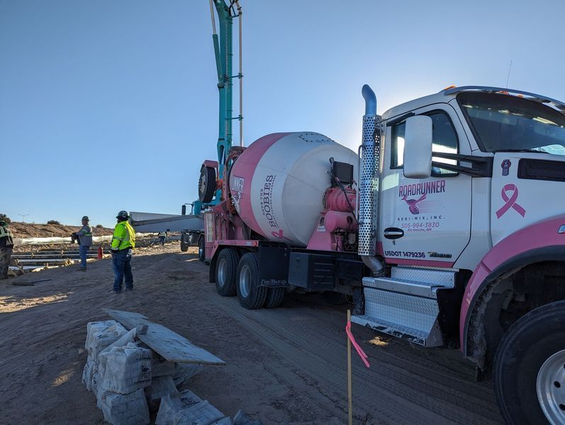 A concrete mixer truck with a pink ribbon on the side is parked on a dirt road.