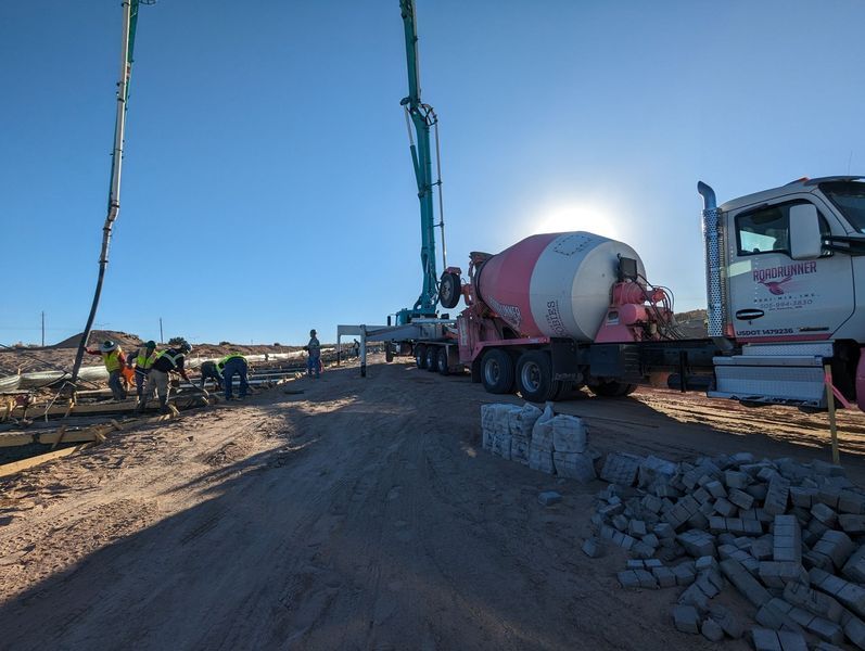 A concrete mixer truck is driving down a dirt road.