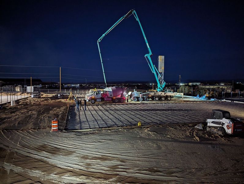A construction site at night with a concrete pump in the background.
