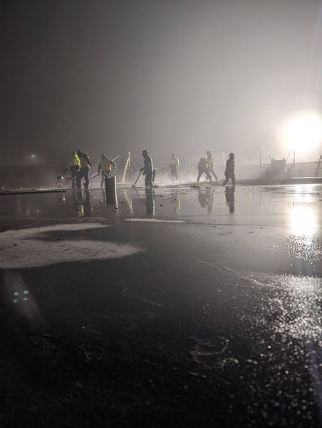 A group of people are spraying water on a wet surface at night.