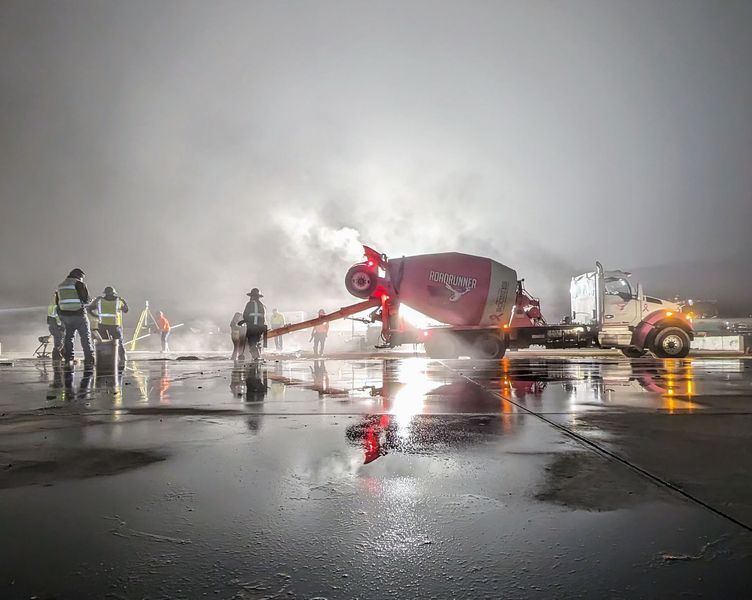 A concrete mixer is being used to pour concrete on an airport tarmac.