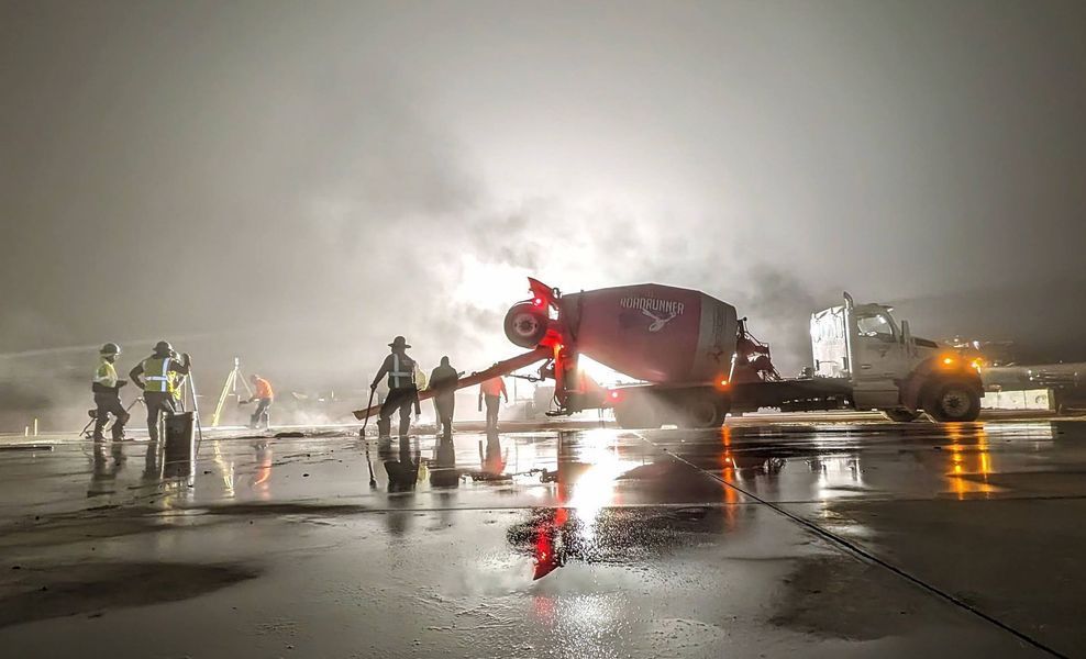 A concrete mixer is pouring concrete on a wet runway at night.
