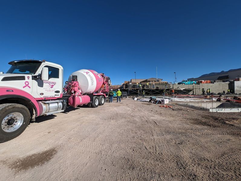 A pink truck with a breast cancer ribbon on the side is parked on a dirt road.