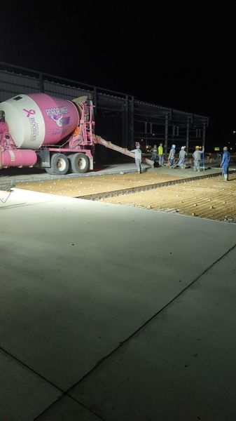 A concrete mixer truck is pouring concrete into a parking lot at night.