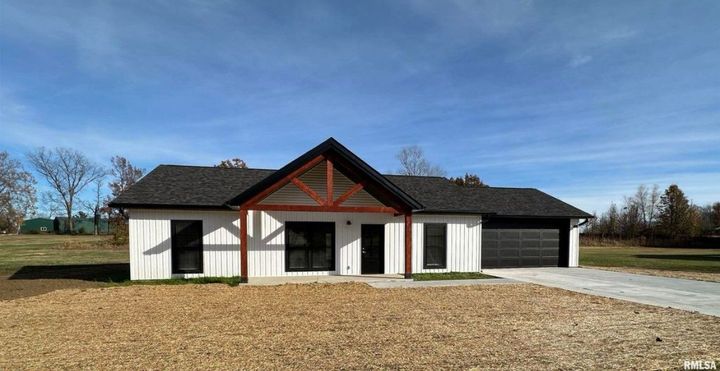 A white house with a black roof is sitting on top of a dirt field.