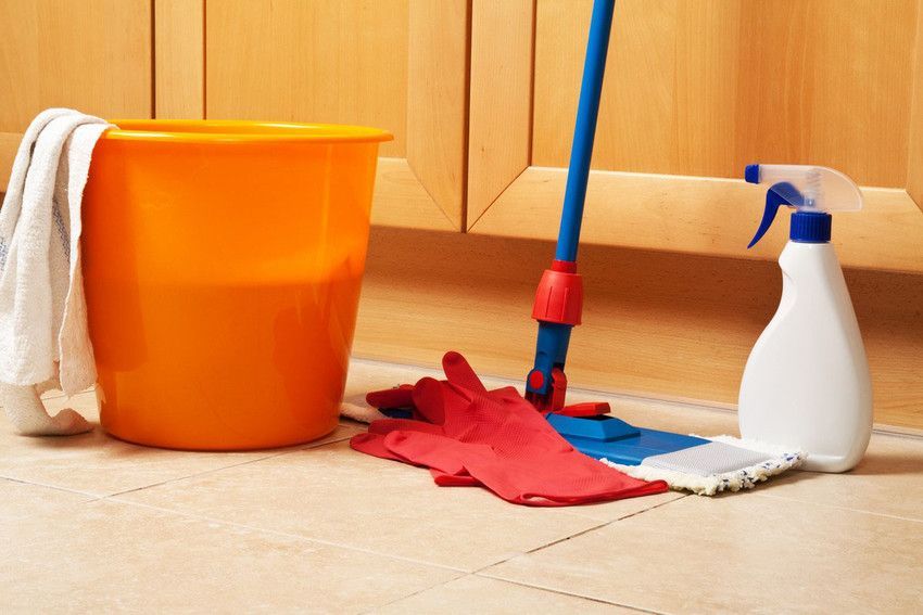 A mop , bucket , and spray bottle are on the floor in a kitchen.