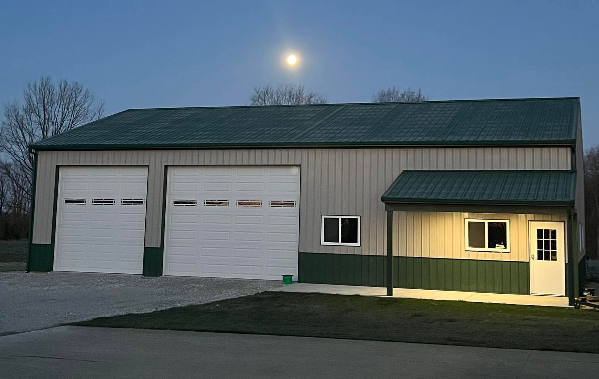 Large garage with two white doors and a lit side entrance at dusk