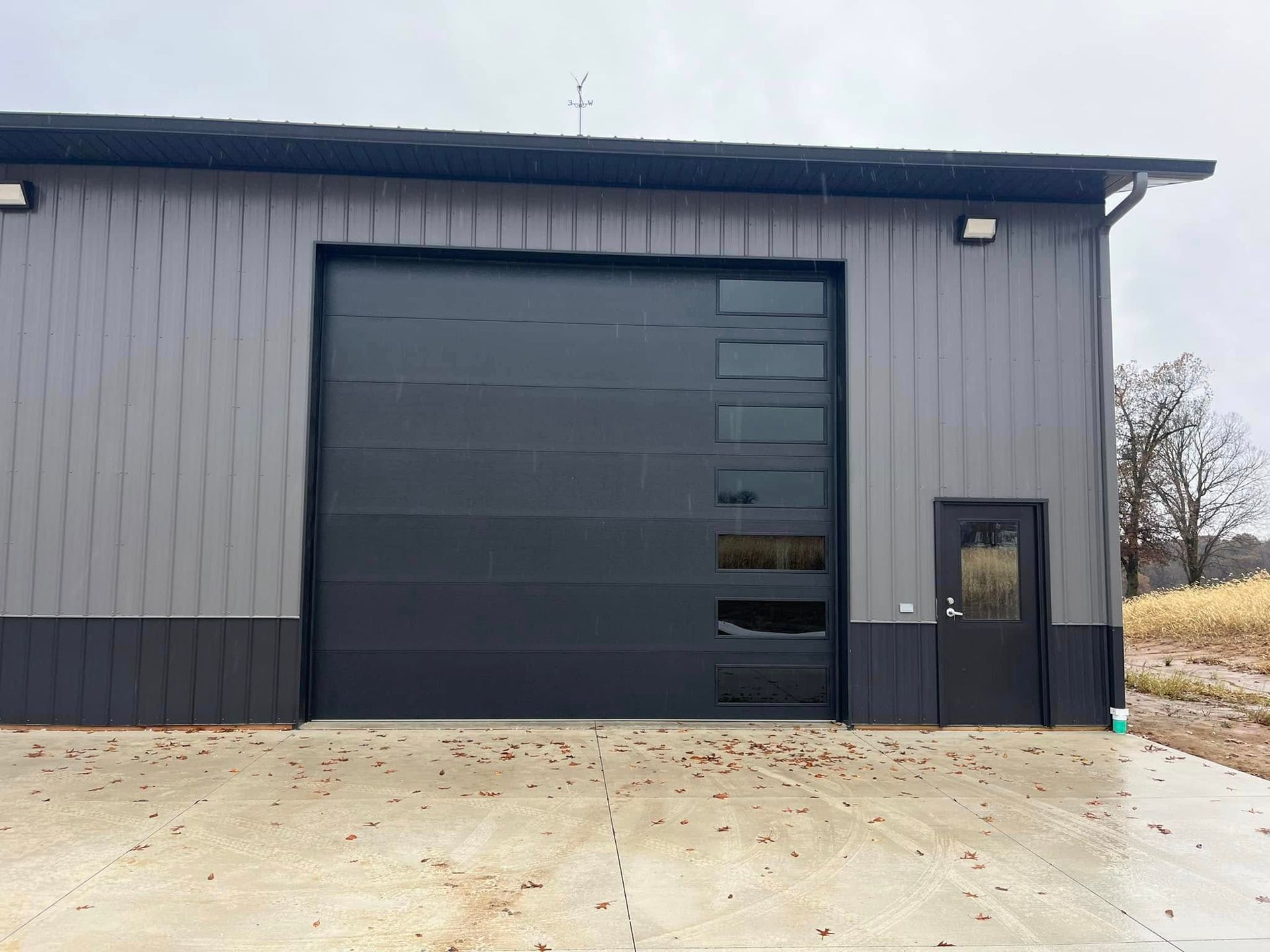 Dark gray industrial building with a large black garage door and a small side entrance.
