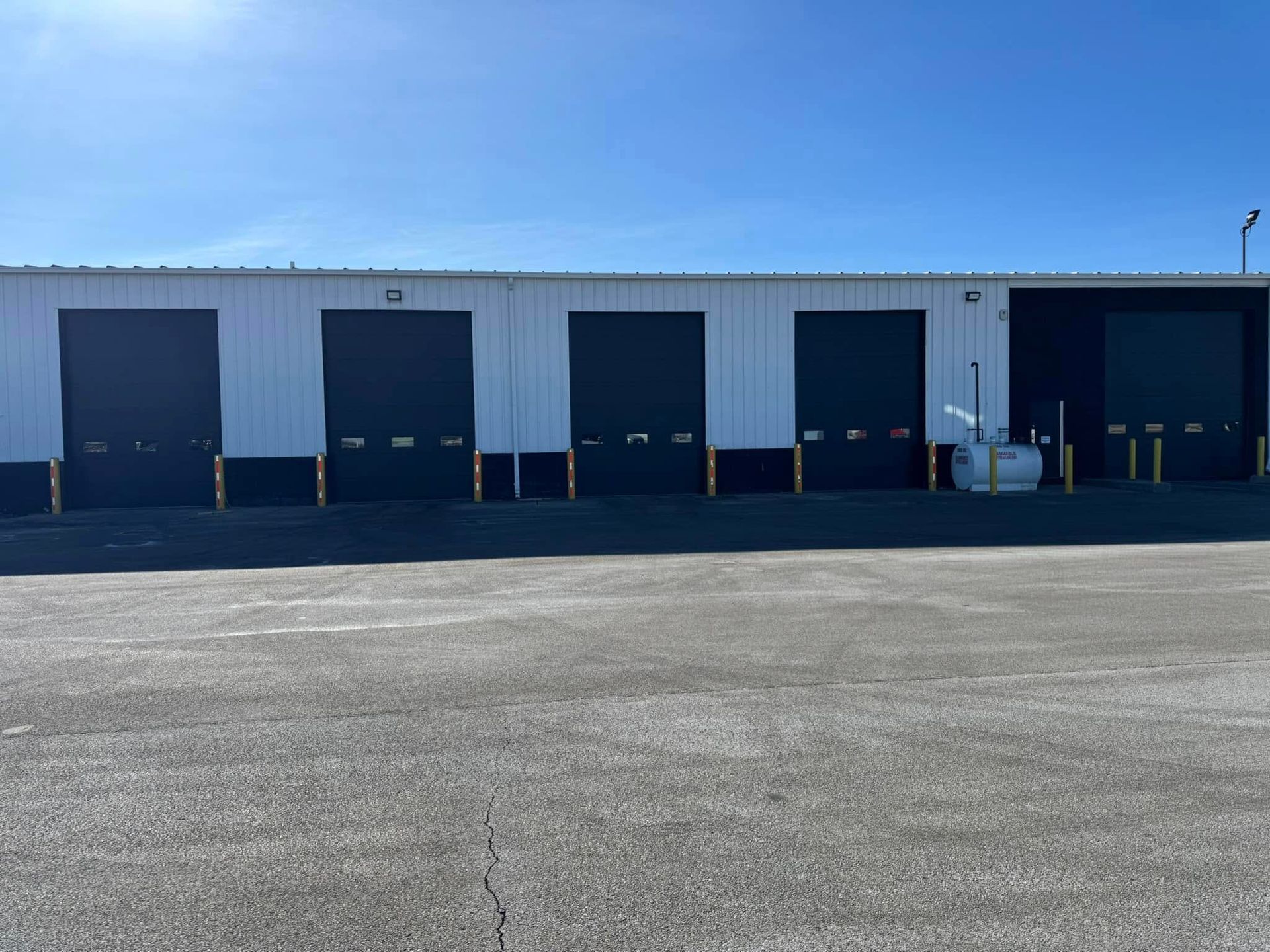 Exterior of a warehouse with several dark loading dock doors on a sunny day