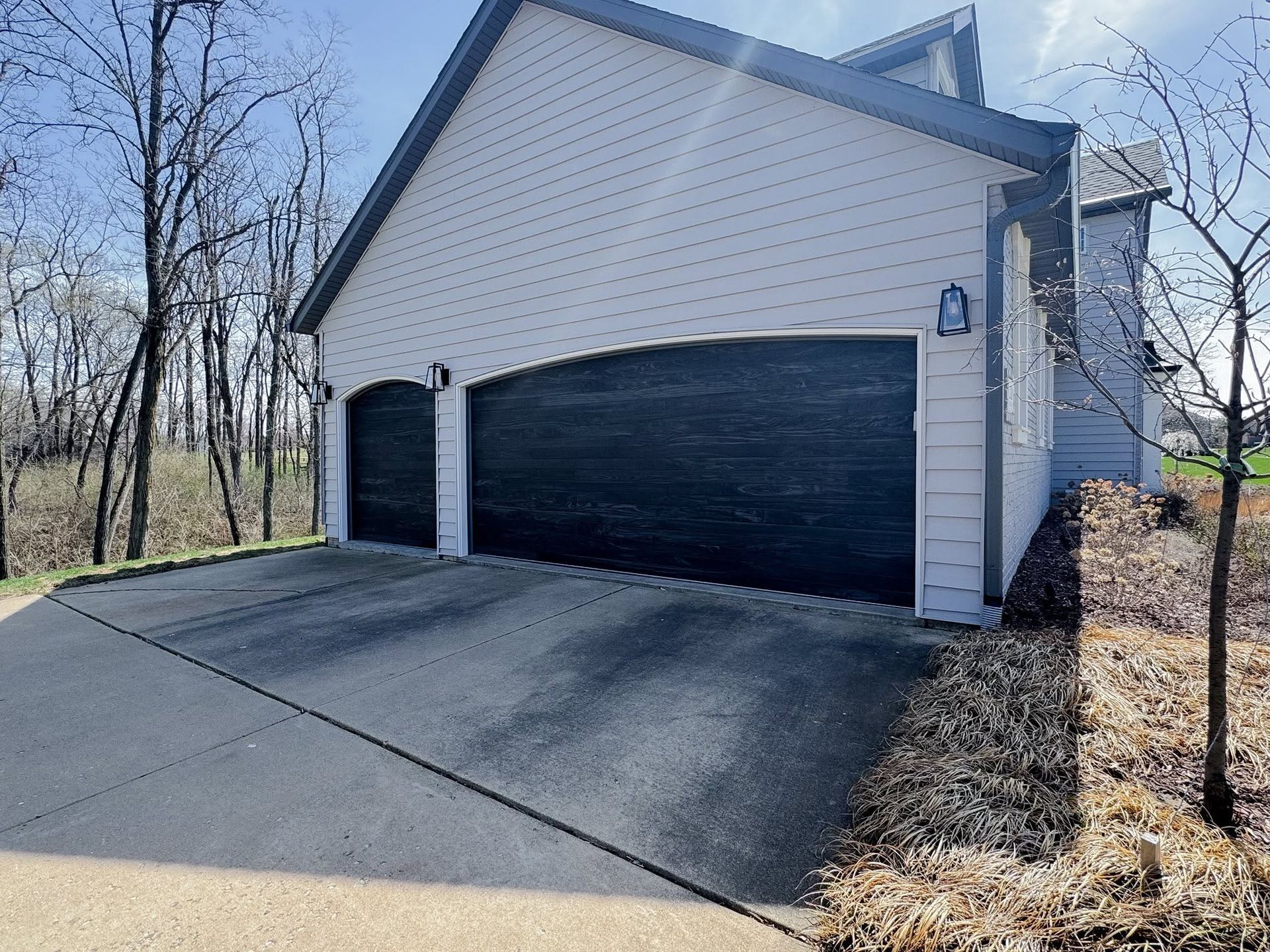 Two-car black garage attached to a white house with a paved driveway