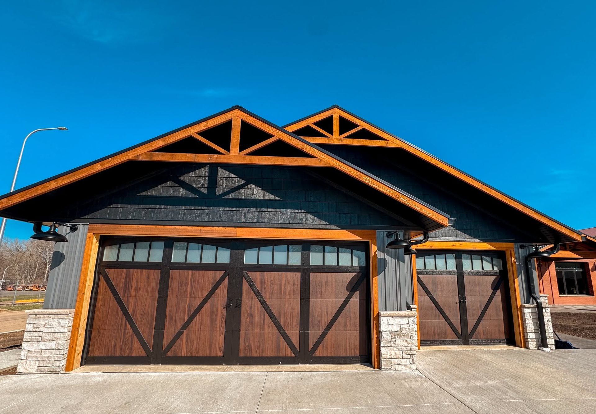 Modern house with dark wood garage doors, stone accents, and a gabled roof under a blue sky