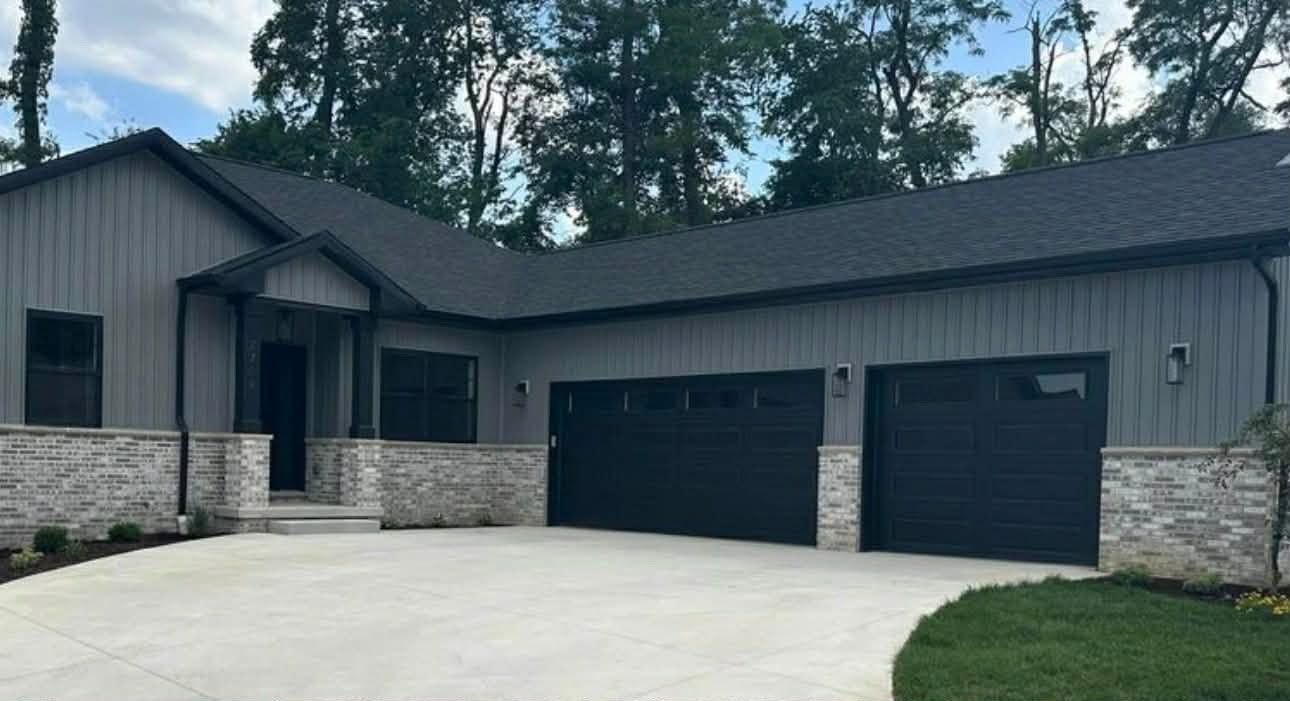 Modern gray single-story house with stone accents, double black garage doors, and a curved concrete driveway