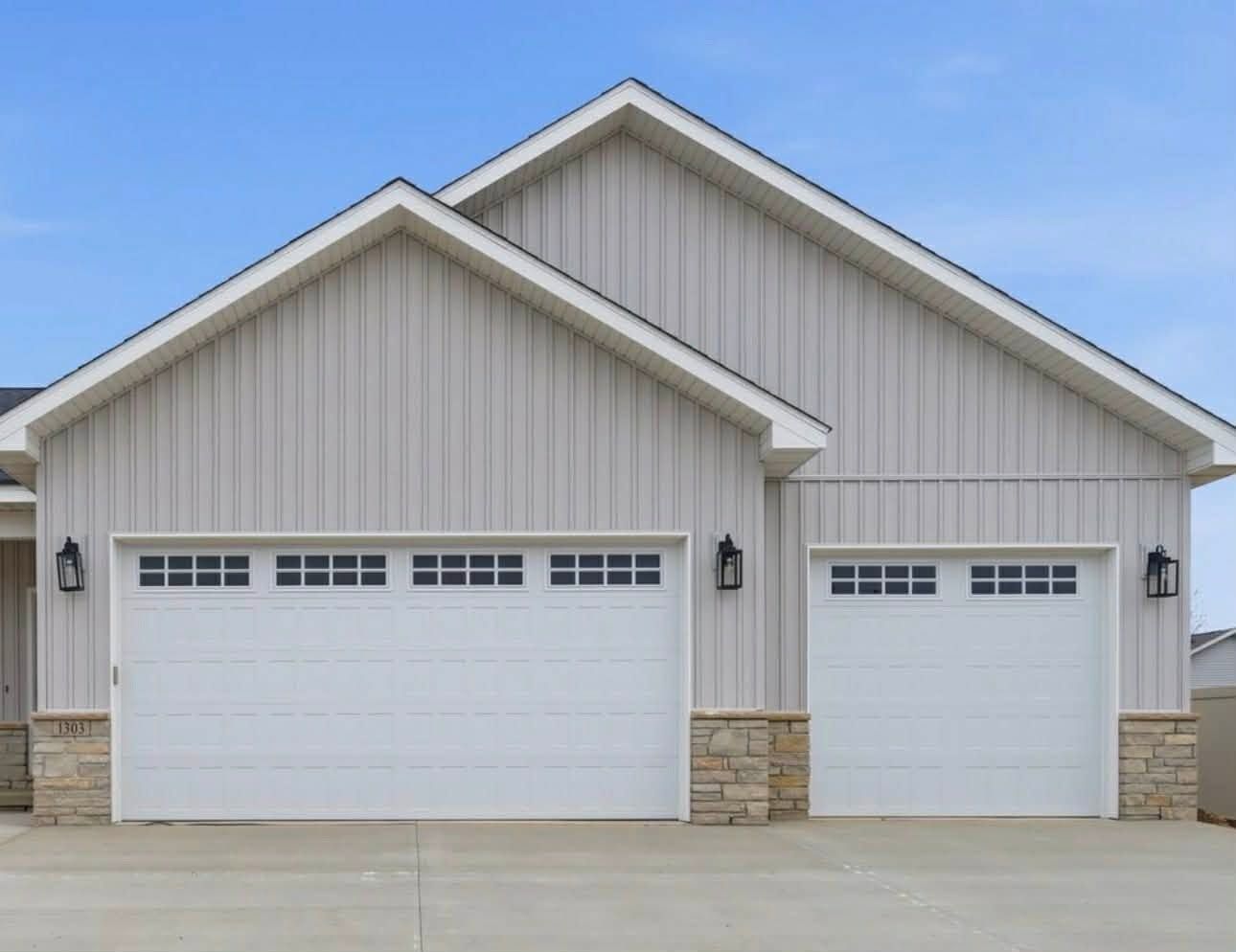 Two-car white garage with beige siding and stone base under a gabled roof.