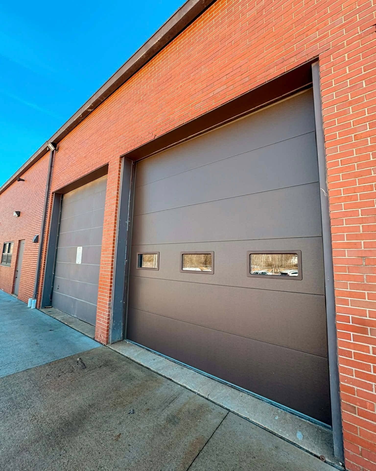 Brick industrial building with two large gray garage doors on a sidewalk under a blue sky