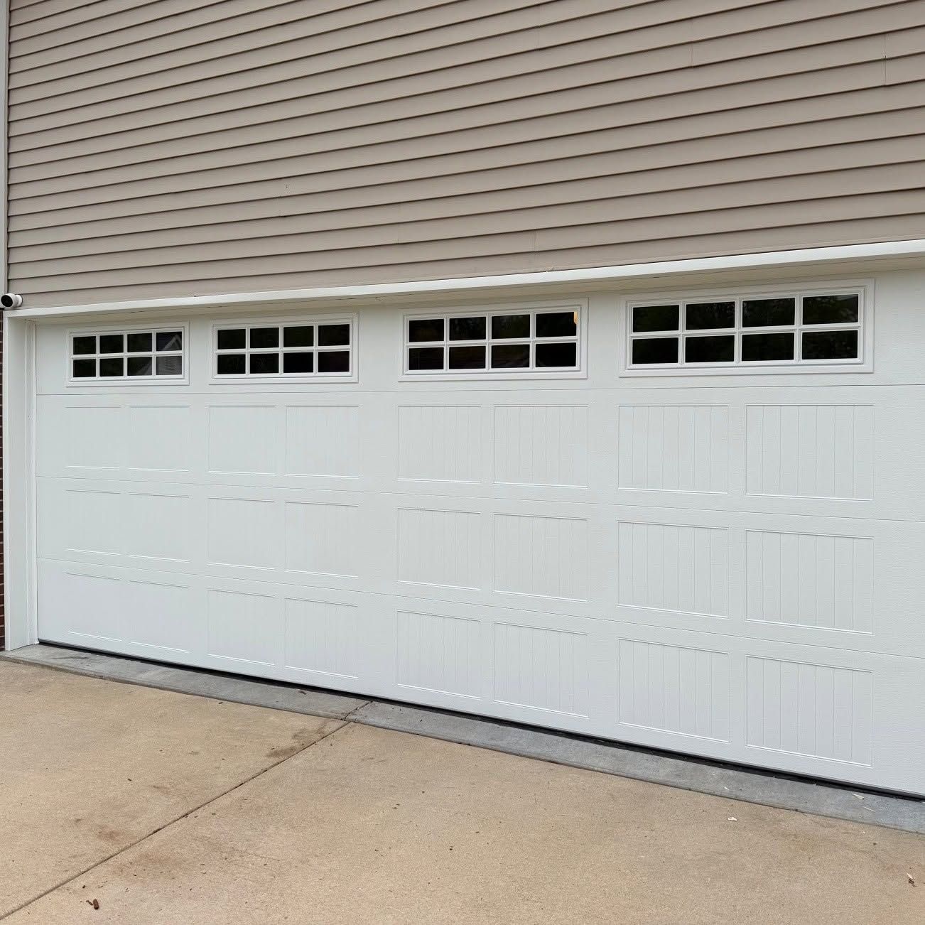 White double garage door with small windows below beige siding on a concrete driveway