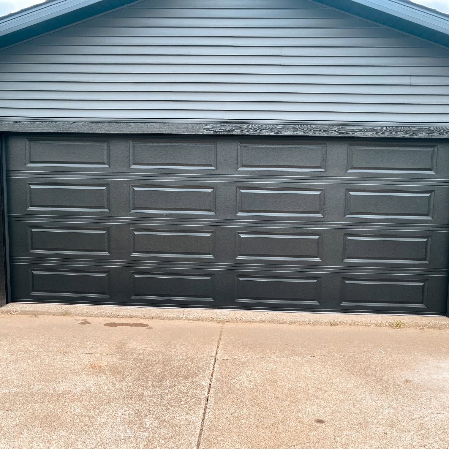 Dark gray garage door on a house with light blue siding and a concrete driveway