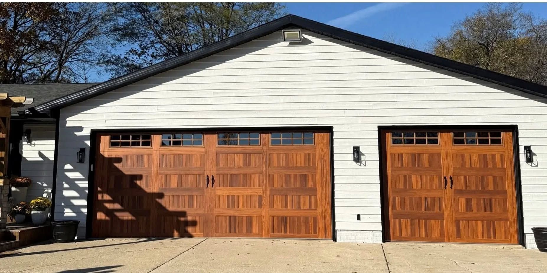 White garage with two wooden doors and a black roof trim, viewed from the front in daylight