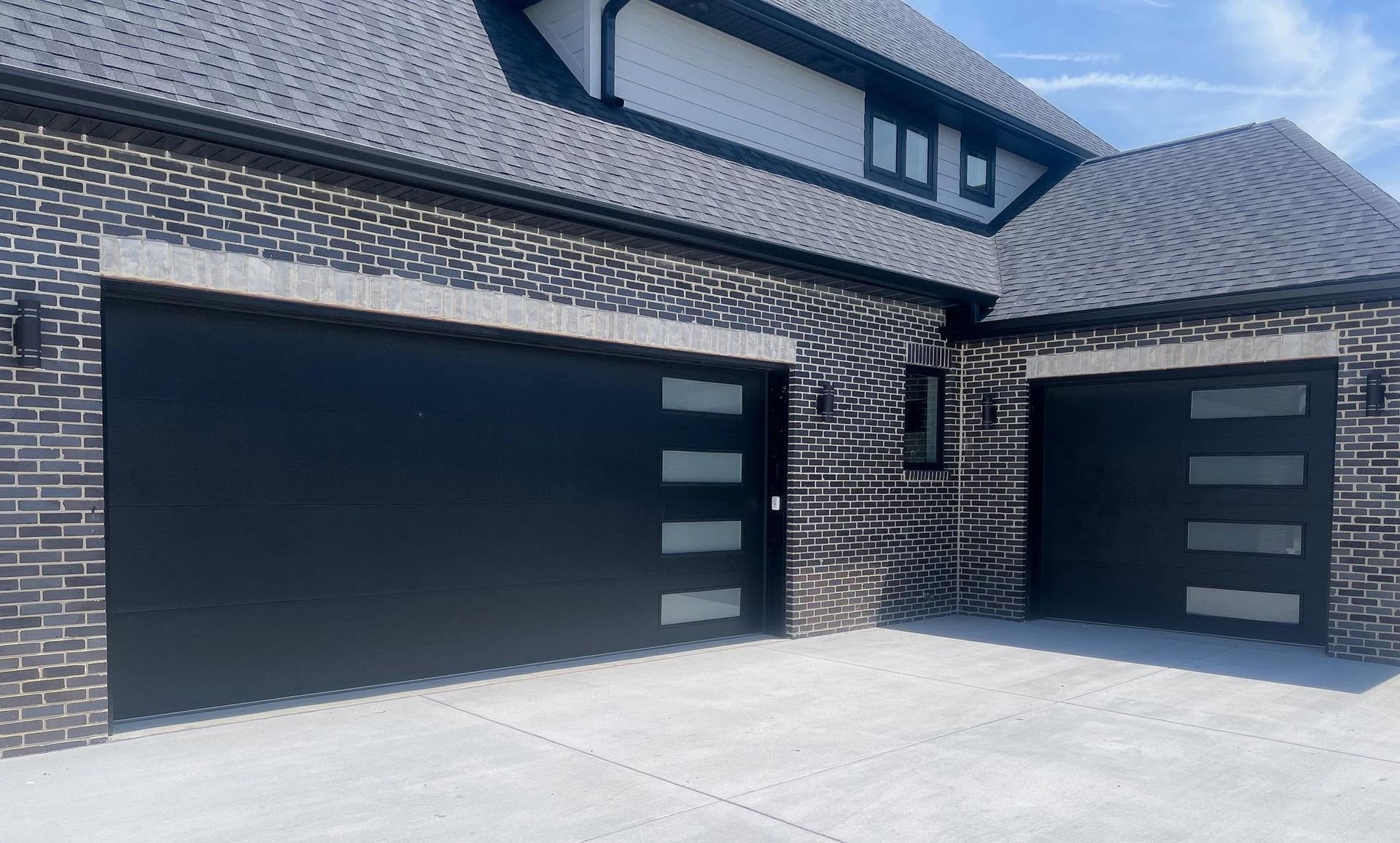 Modern brick house exterior with black garage doors and a concrete driveway