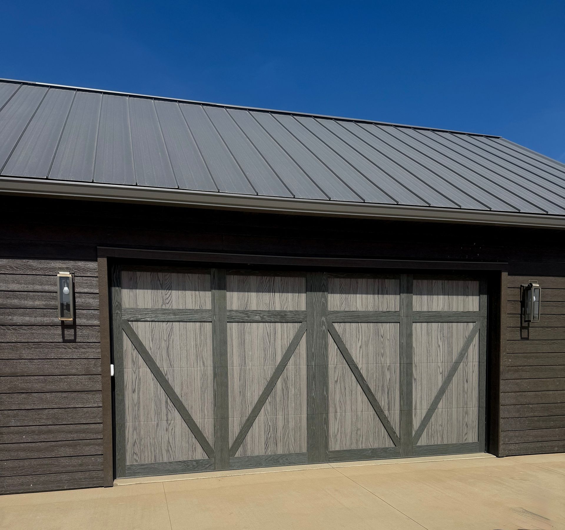Gray barn-style garage with large wooden doors and a metal roof under a blue sky