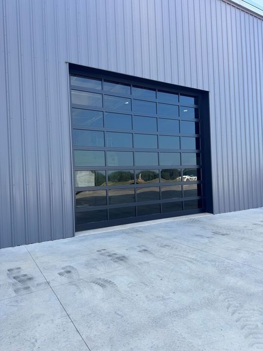 Large glass garage door set in a gray corrugated metal building. Concrete in front.