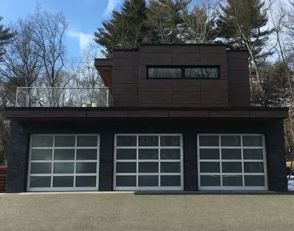 Modern garage with three glass doors, dark facade, and rooftop deck under a blue sky.
