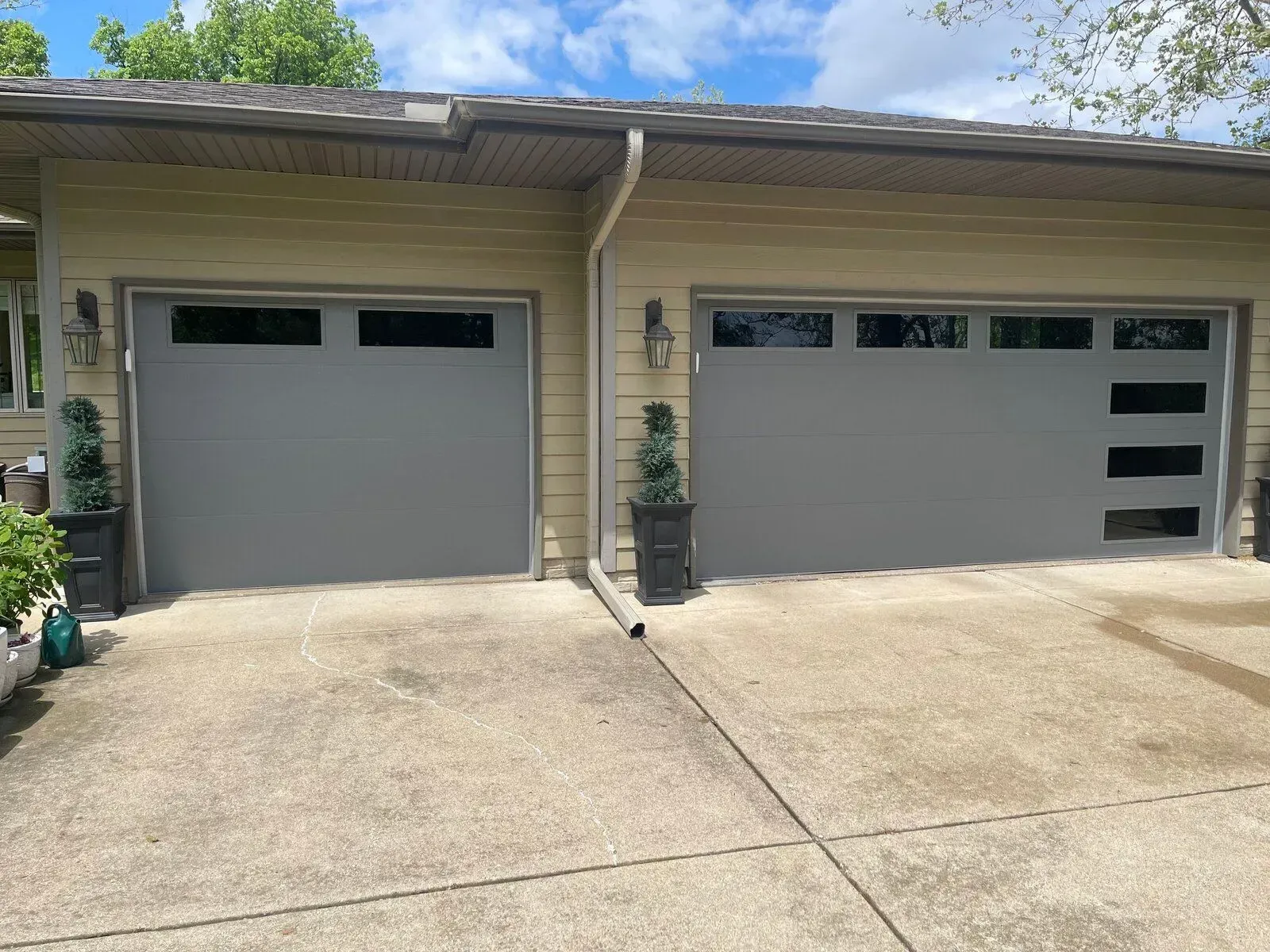 Two gray garage doors with windows on a light yellow house, with concrete driveway.