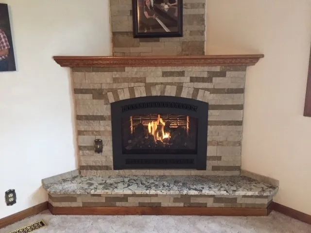Stone fireplace with a lit fire, brick mantel, and tiled hearth in a living room