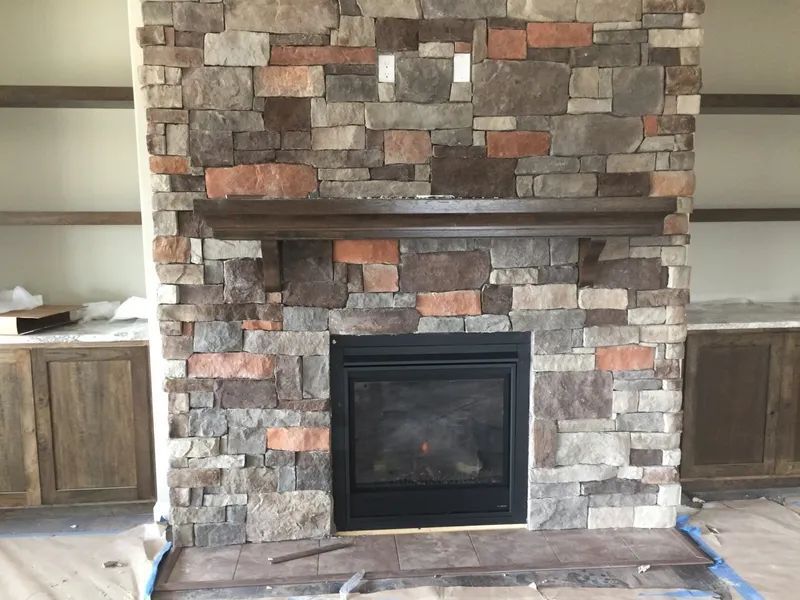 Stone fireplace with dark insert and wooden mantel in a partially finished room, flanked by built-in cabinets